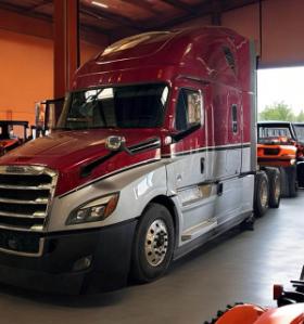 A front shot of the Chemeketa Diesel Technology programs Freightliner Diesel semitruck in the garage lab. The top half of the truck is painted red, the bottom half is painted light gray.