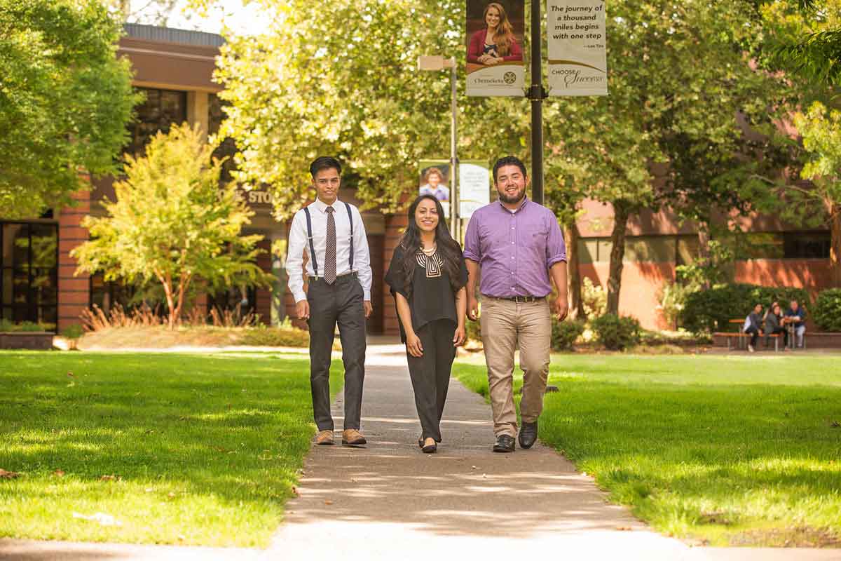 Three people walk through the center of campus on a sunny day